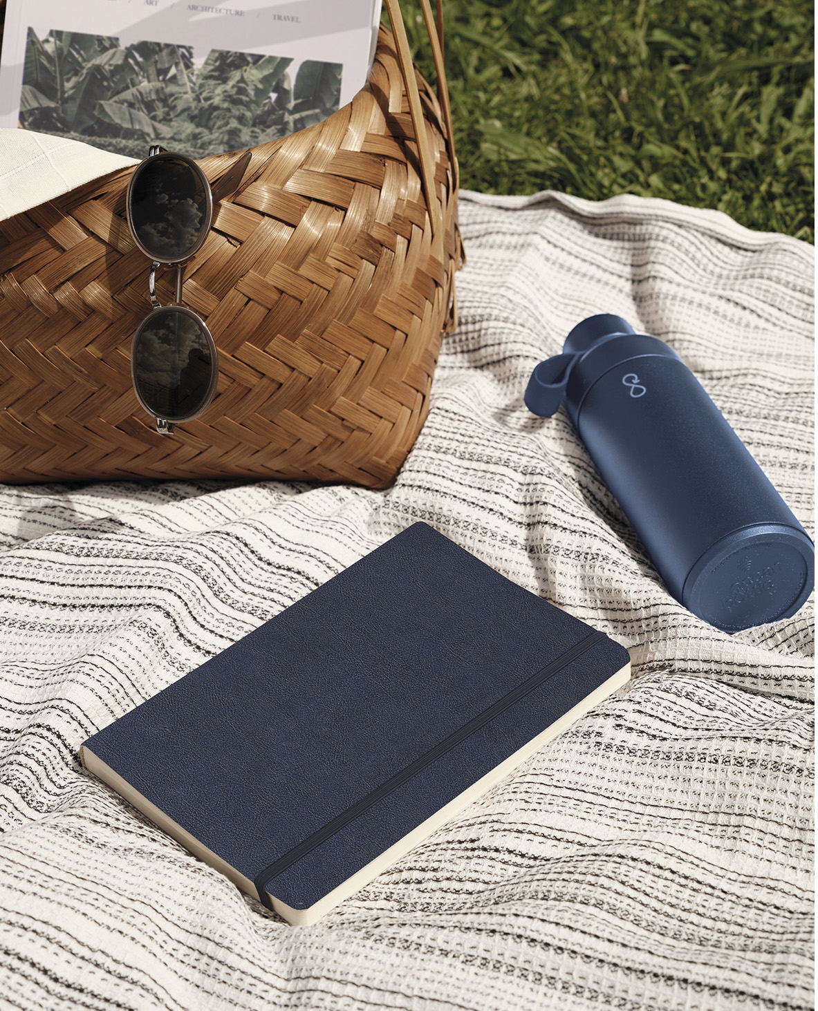 A notebook on a pic nic blanket with a basket and a bottle